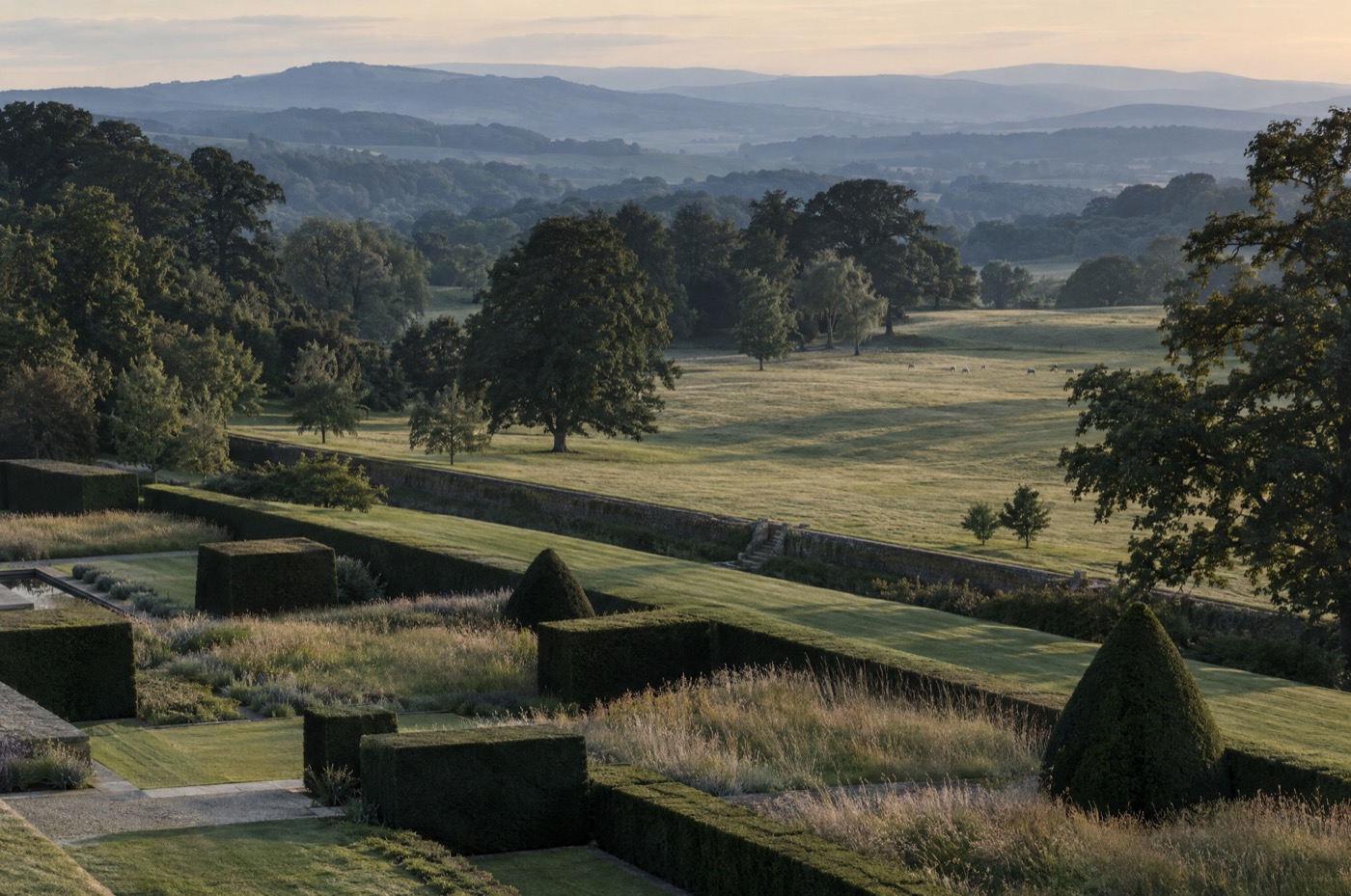 An elevated evening view across an estate landscape of clipped yew and meadow grass.