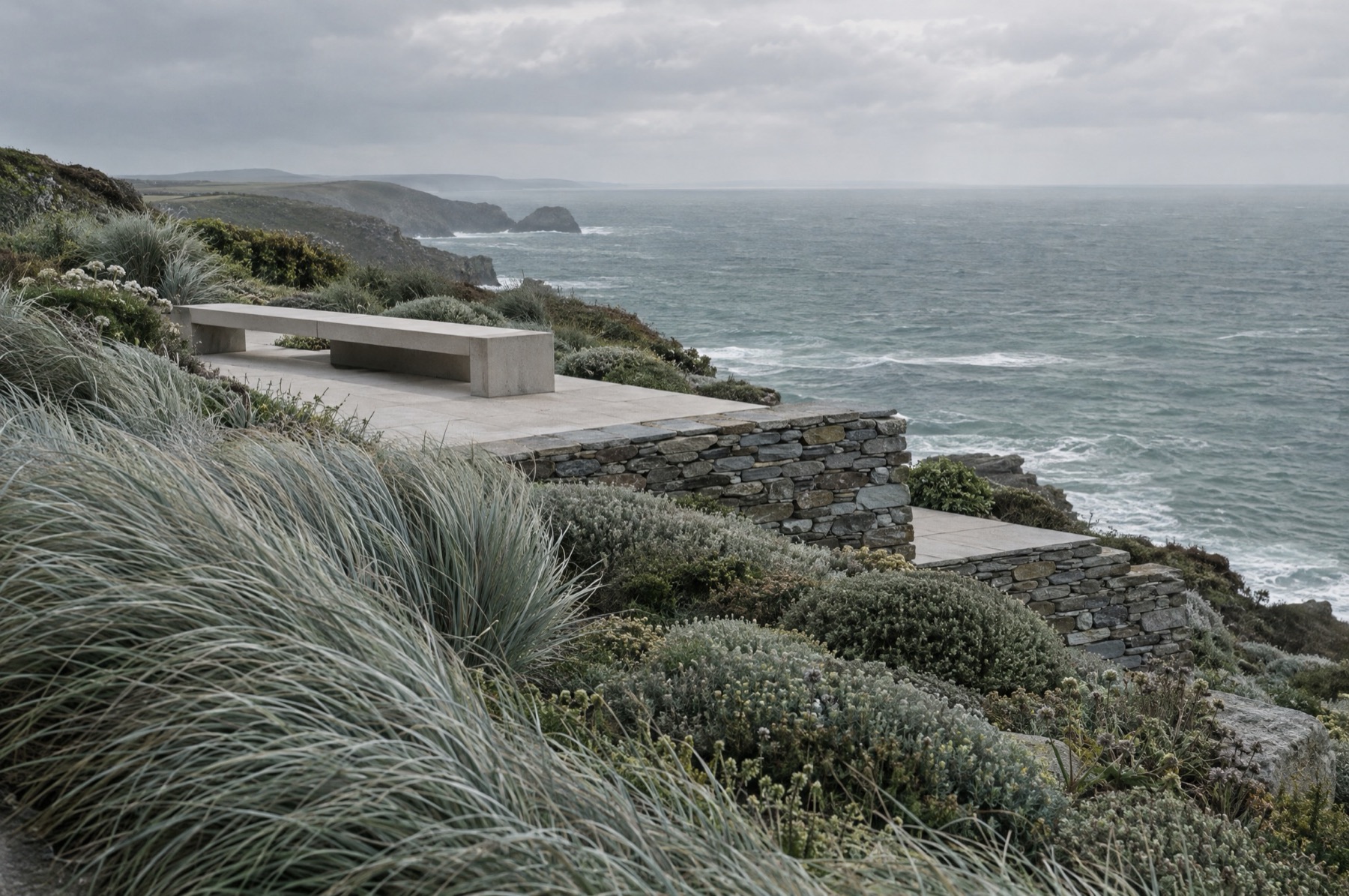A clifftop coastal garden with windswept silver-blue grasses, a slate retaining wall and the Atlantic beyond.